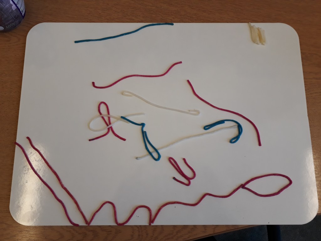 Picture of a student’s graphic score created using wax sticks on a white board. It has different coloured shapes which are mostly wiggly lines in different directions. 